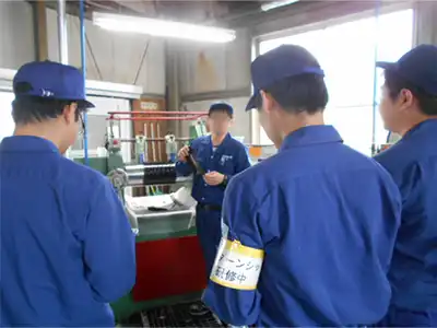 青い作業着と防止を着用し、工場内で説明を受けているインターンシップ参加者